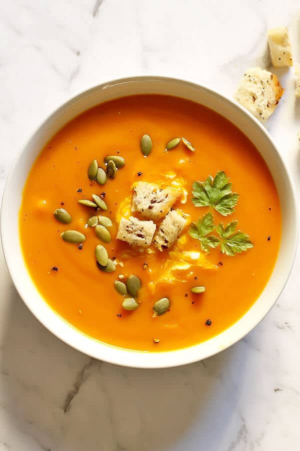 a bowl of roasted pumpkin and sweet potato soup topped with seeds and croutons
