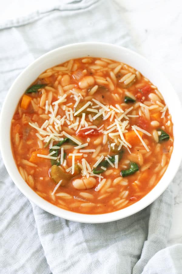 italian vegetable orzo soup in a white bowl of a grey napkin