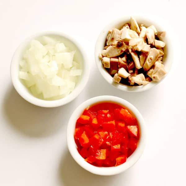 3 small white bowls sitting on top a white tabletop, filled with diced mushrooms, onions and capsicum.