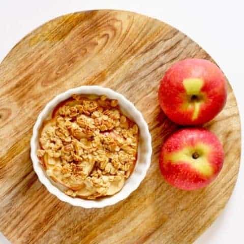 apple crisp sitting on wooden cutting board next to two red apples