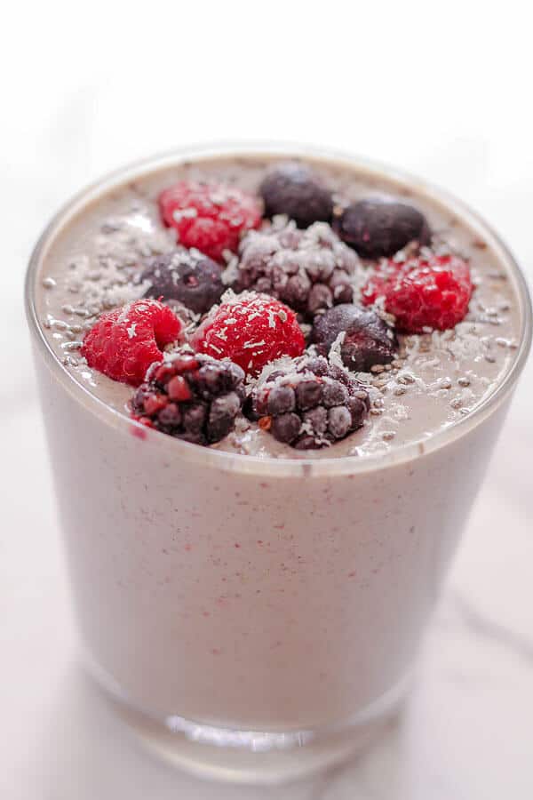 berry green smoothie in a small glass topped with berries and desiccated coconut