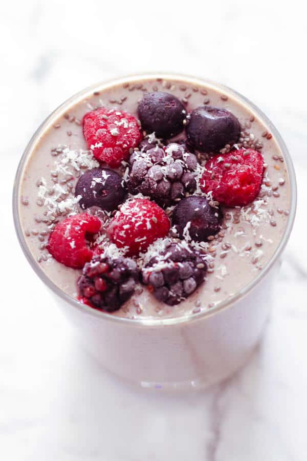 berry green smoothie in a small glass topped with berries and desiccated coconut