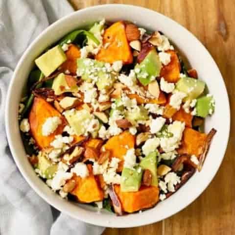 roasted sweet potato, avocado and feta salad in a white bowl on top of a wooden cutting board