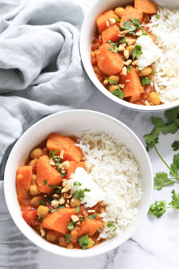 two bowls of sweet potato, lentil & chickpea curry next to a grey napkin and coriander leaves