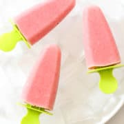 3 strawberry pineapple popsicles on a plate filled with ice cubes.