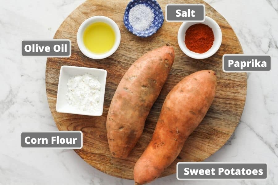 sweet potato wedges ingredients on a wooden board including oil and corn flour.