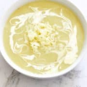Potato and Leek Soup in a white bowl covered in heavy cream swirls.