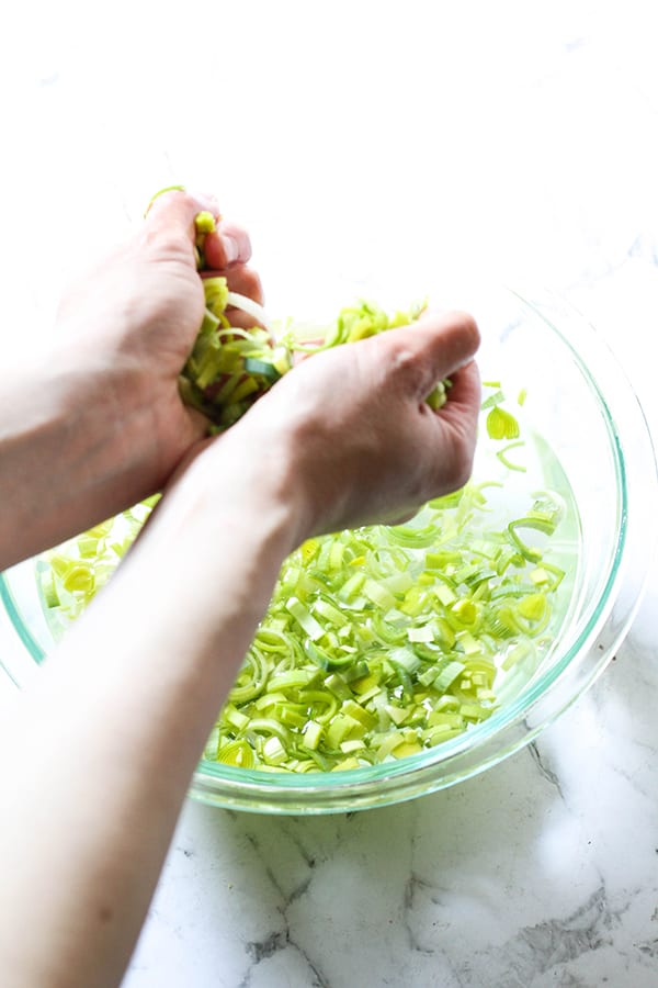 hands removing handfuls of sliced leeks from a mixing bowl filled with water.