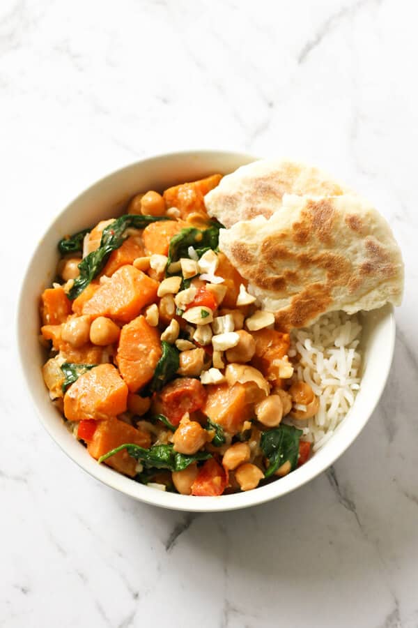 sweet potato, chickpea and spinach curry in a bowl with rice surrounded by vegetables