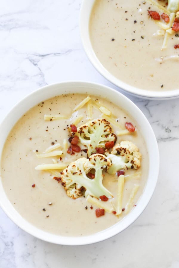 cauliflower and bacon soup in a white bowl topped with bacon bits and roasted cauliflower pieces