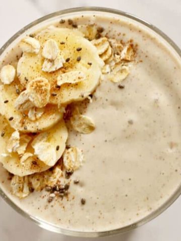 banana oat smoothie close up topped with banana slices, rolled oats, cinnamon and chia seeds