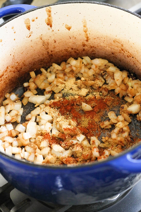 onion, garlic and spices in a blue dutch oven.