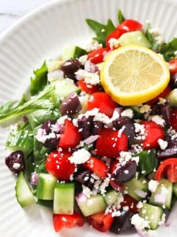 close up image of greek salad topped with lemon slice