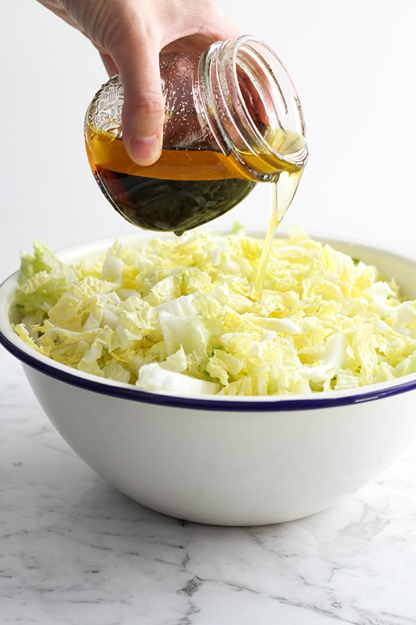a hand pouring salad dressing over a bowl of salad.