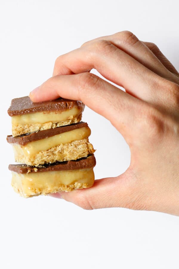 a hand holding 3 pieces of chocolate caramel slice stacked