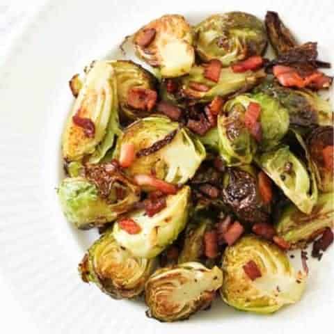 a plate of roasted brussels sprouts with bacon on a white plate