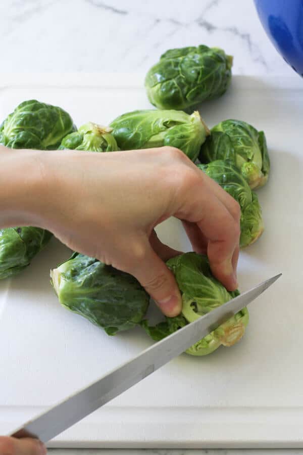 a hand demonstrating how to trim the ends of brussels sprouts