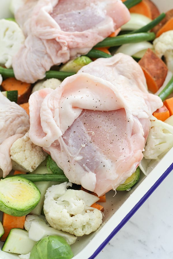 chicken thighs laying skin side up on a tray of vegetables with the skin peeled back