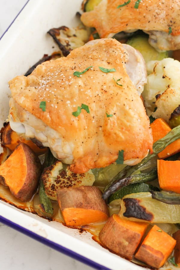 crispy baked chicken thighs on a baking tray with vegetables.