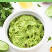 healthy guacamole in a white bowl surrounded by ingredients.