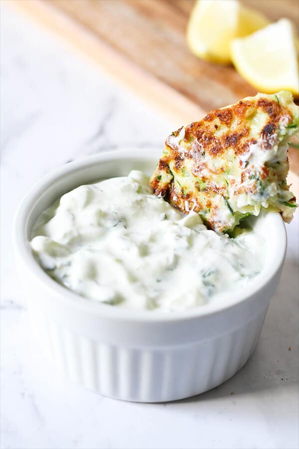 Greek Tzatziki dip in a white bowl with a fritter partially submerged
