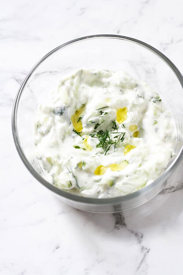 Greek Tzatziki in a glass bowl with olive oil and chopped dill on top