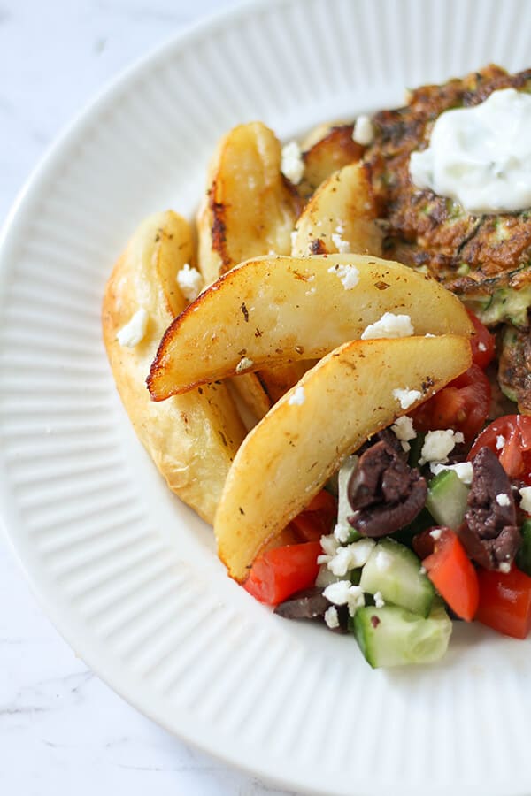 greek lemon potatoes on a plate with greek salad and fritters