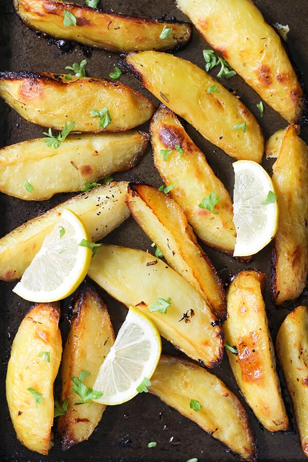 greek potatoes on a baking tray with lemon slices and parsley on top