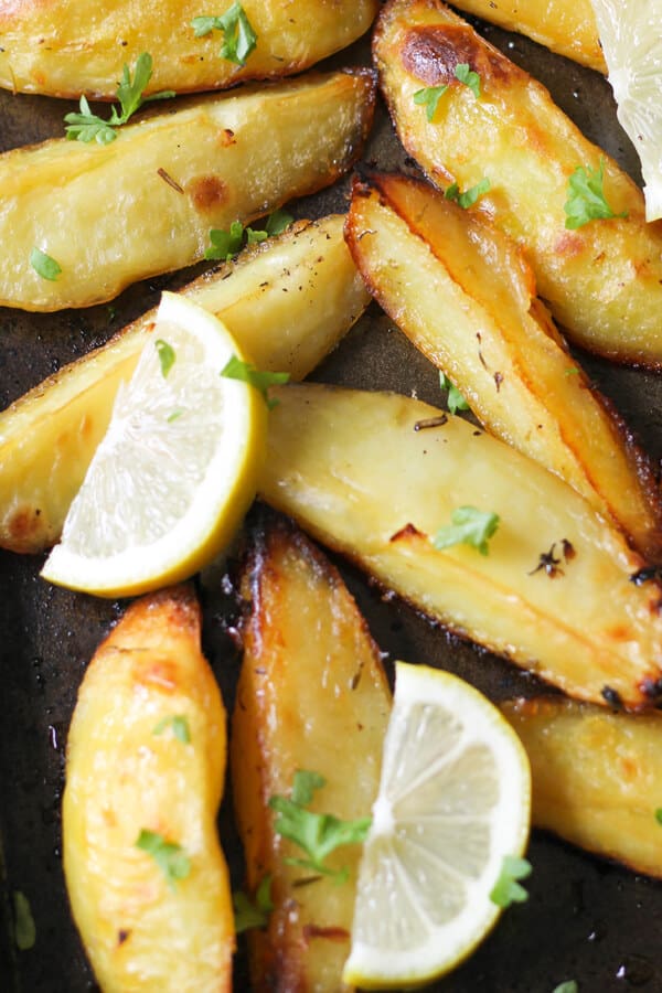 greek potatoes on a baking tray with lemon slices and parsley on top