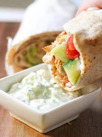 hand dipping a chicken gyro into a bowl of tzatziki sauce