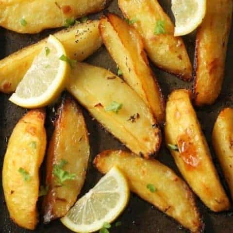 greek potatoes on a baking tray with lemon slices and parsley on top.