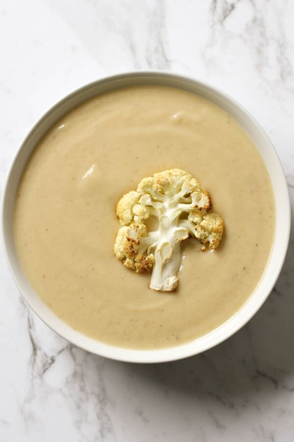 a bowl of cauliflower soup with roasted cauliflower, shredded cheese and parsley on top.