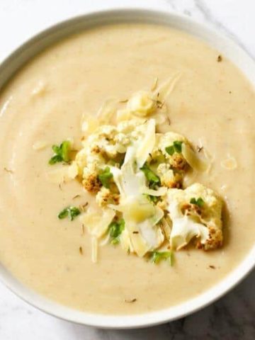 a bowl of cauliflower soup with roasted cauliflower, shredded cheese and parsley on top.
