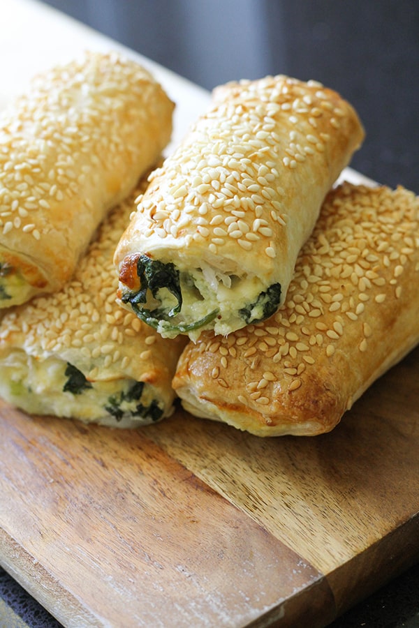 spinach ricotta rolls stacked on top of each other on a wooden board.