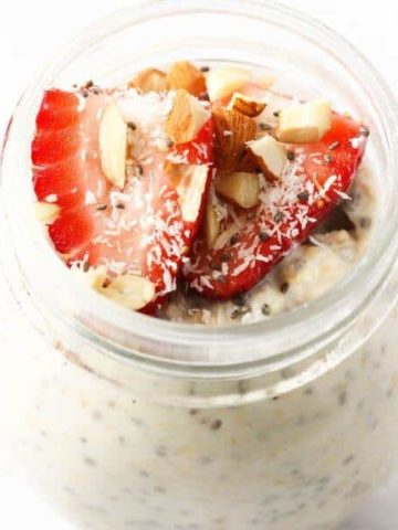 jar of overnight oats topped with strawberries, shredded coconut and almonds.
