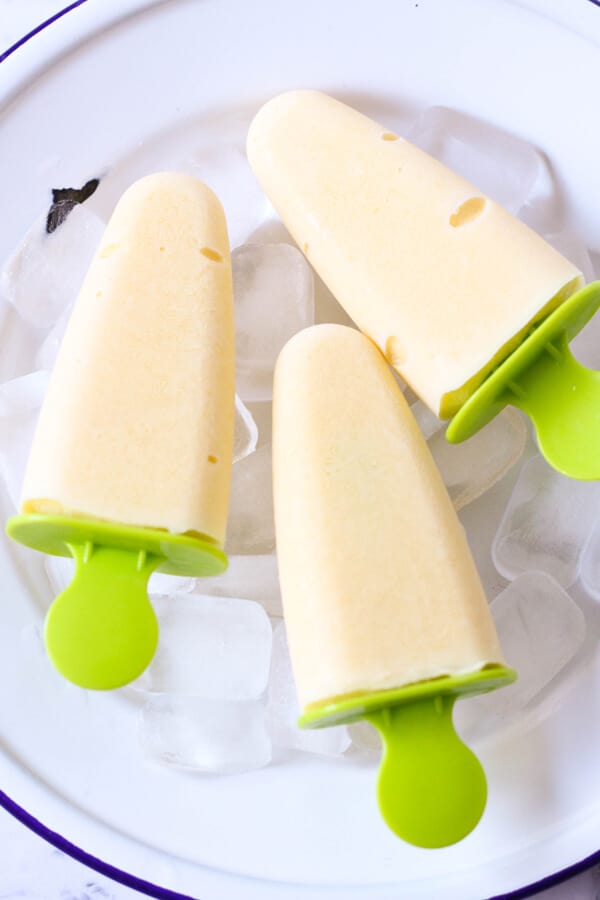 3 mango popsicles on a bed of ice cubes. 