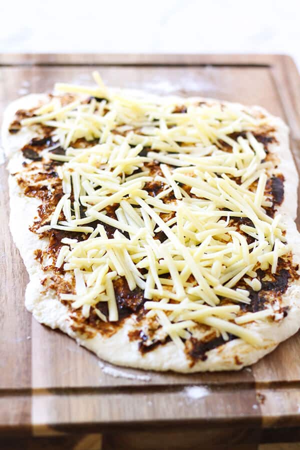 dough rolled out of a wooden cutting board topped with vegemite and cheese.