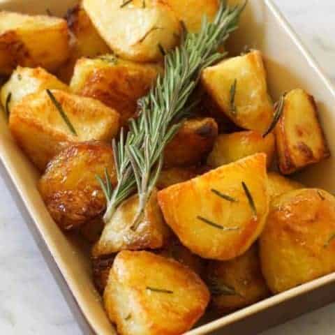 Crispy roast potatoes in a serving tray with rosemary sprigs on top.