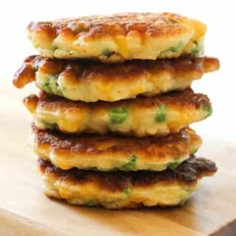Pea & Sweet Corn Fritters stacked on top of each other on a wooden board.