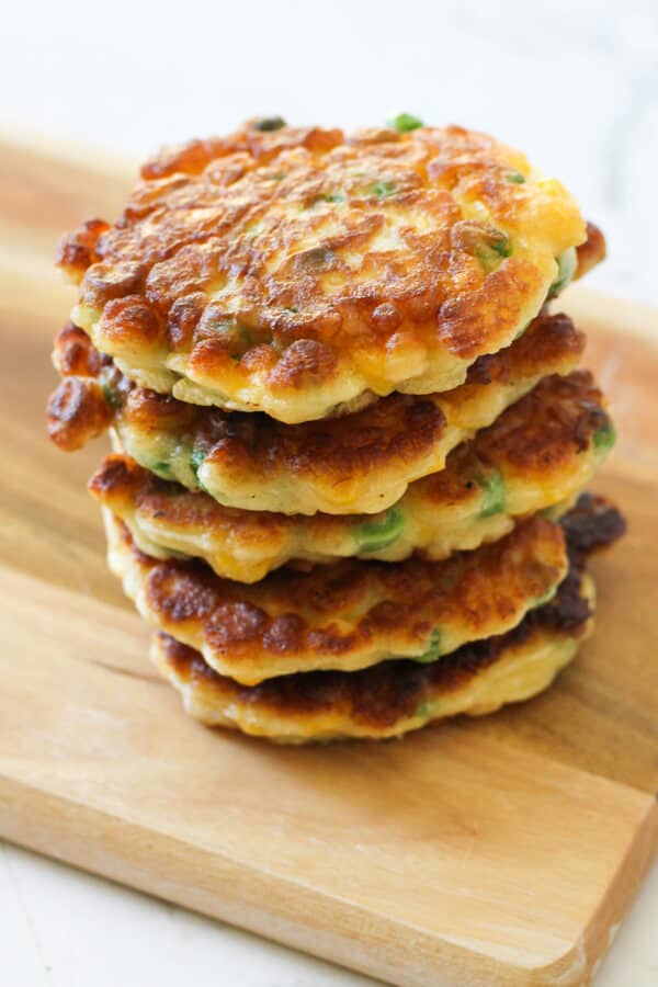 Pea & Sweet Corn Fritters stacked on top of each other on a wooden board.