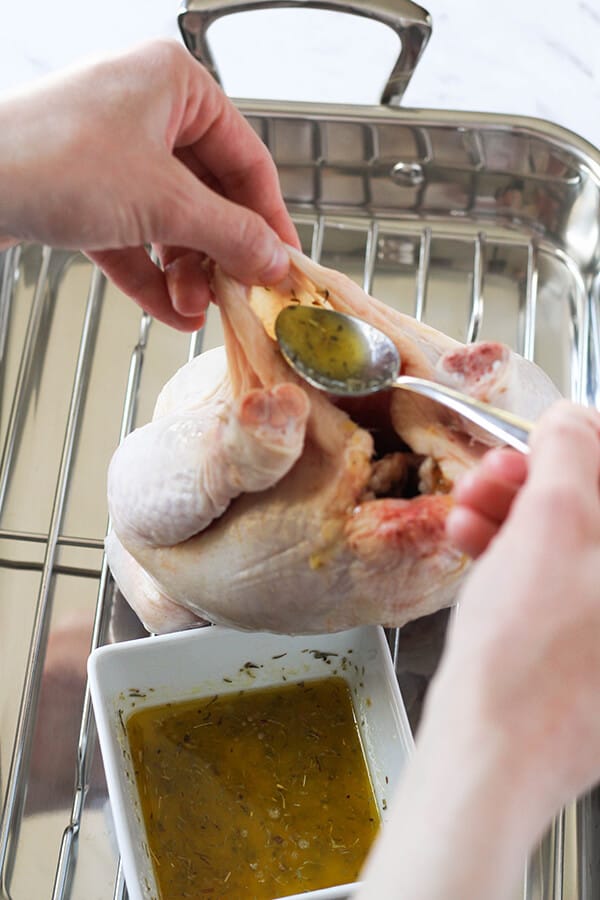 hands pouring lemon butter under the skin of a whole chicken. 