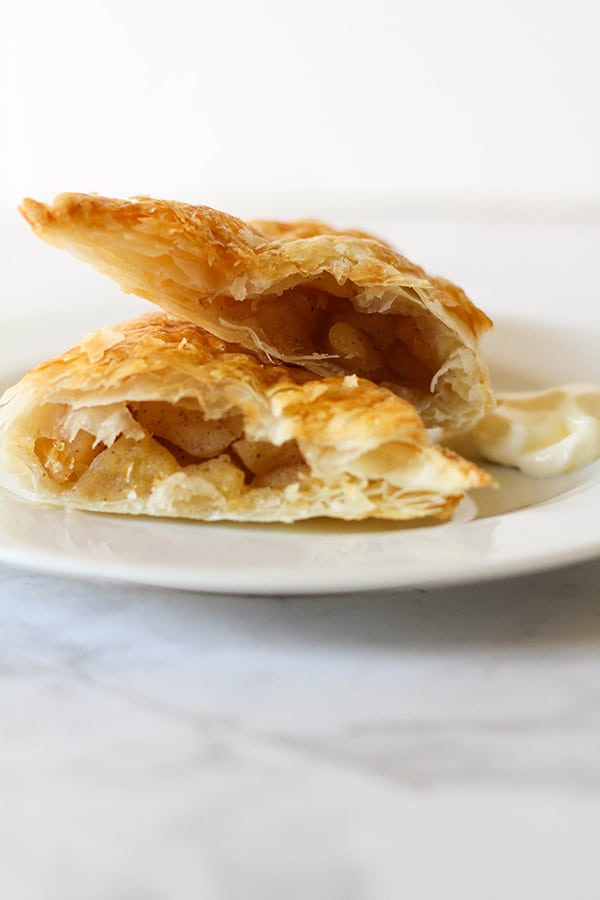 apple turnover broken into halves on a white plate.