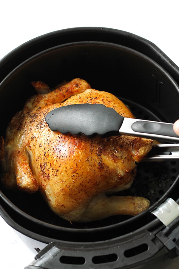whole chicken sitting in an air fryer basket being grabbed with tongs.