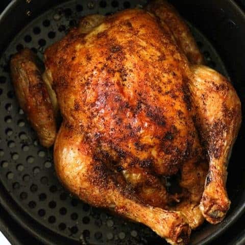 Whole roast chicken sitting in air fryer basket.