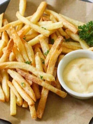 French fries on a grey plate with a bowl of aioli.