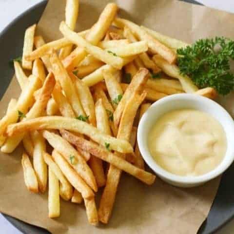 French fries on a grey plate with a bowl of aioli.