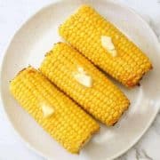 3 corn on the cob on a white plate.