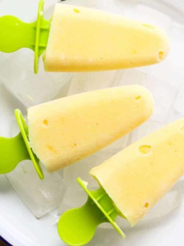 mango pineapple popsicles on a white plate covered in ice cubes.
