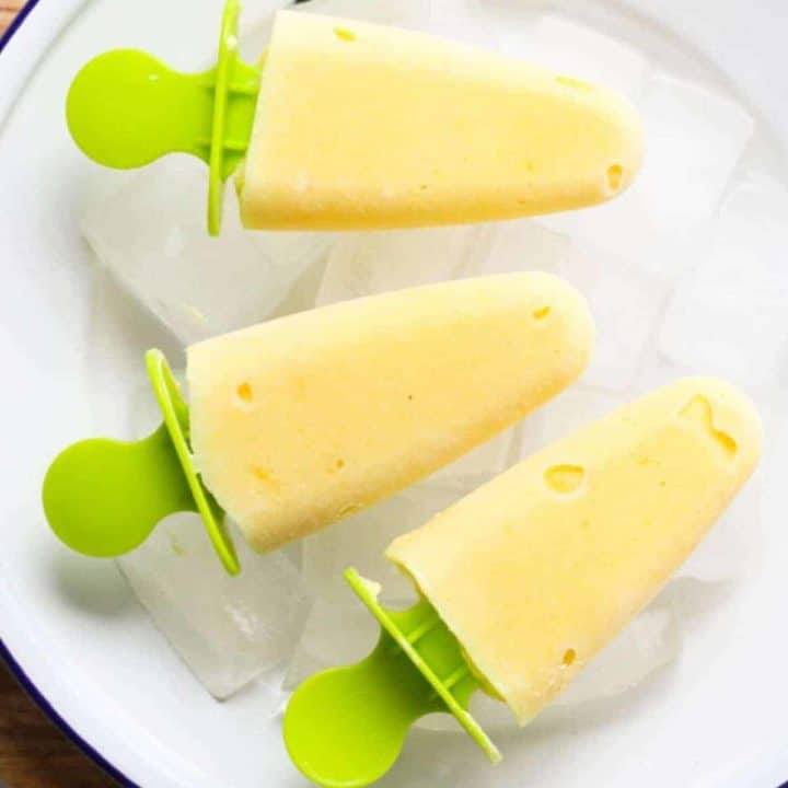 mango pineapple popsicles on a white plate covered in ice cubes.