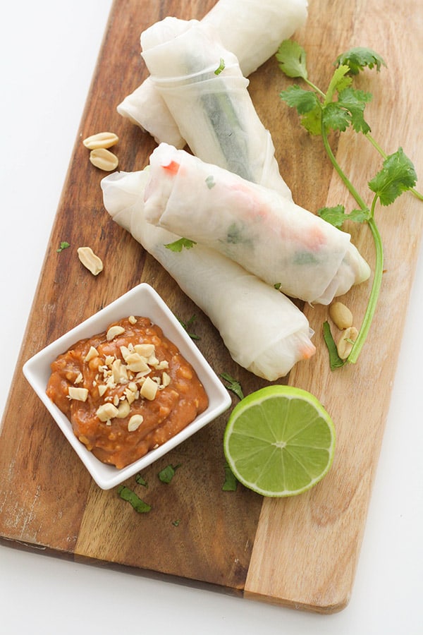 peanut hoisin sauce in a small square white bowl on a wooden board with rice paper rolls.